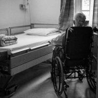 A man in a wheelchair looks at his hospital bed in his hospital room.