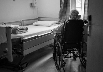 A man in a wheelchair looks at his hospital bed in his hospital room.
