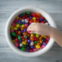 A hand picking up brightly colored candies out of a bowl