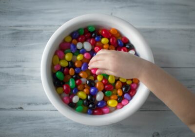 A hand picking up brightly colored candies out of a bowl