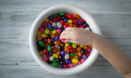 A hand picking up brightly colored candies out of a bowl