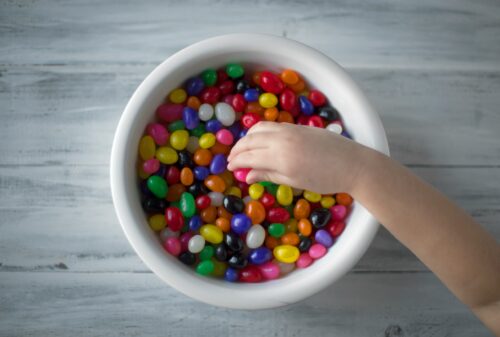 A hand picking up brightly colored candies out of a bowl