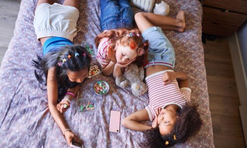 children lying on a bed, using their phones and eating junk food