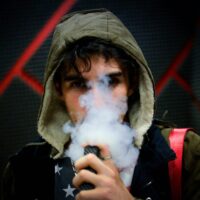 a boy vaping, the lower part of his face obscured by smoke