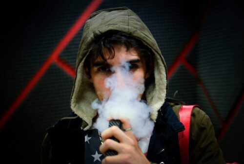 a boy vaping, the lower part of his face obscured by smoke