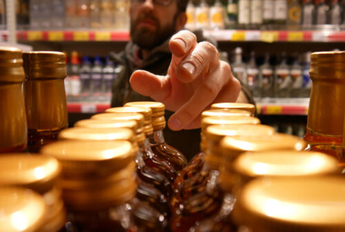 A man reaches out to get a bottle of liquor in a liquor store