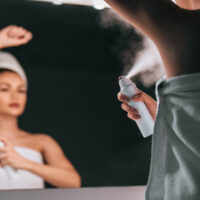 A woman spraying herself with a personal care product