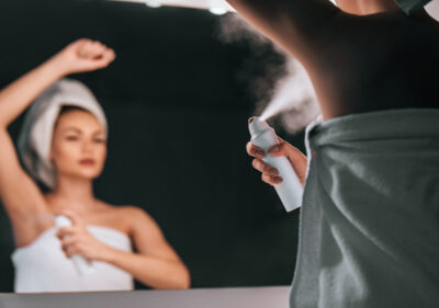 A woman spraying herself with a personal care product
