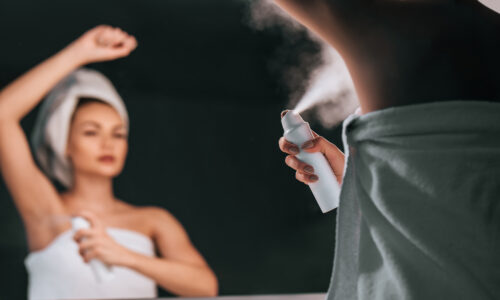 A woman spraying herself with a personal care product