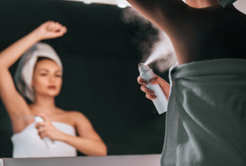 A woman spraying herself with a personal care product