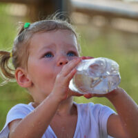 A young girl drinks water from a plastic water bottle