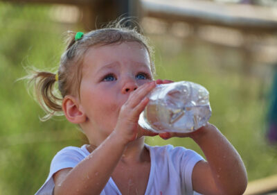A young girl drinks water from a plastic water bottle