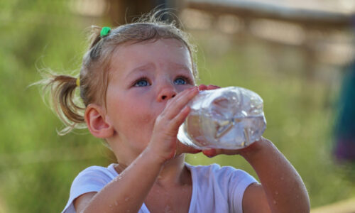 A young girl drinks water from a plastic water bottle