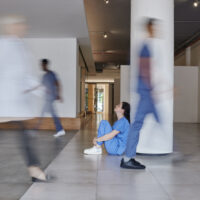 A worried nurse sits on the floor of a hospital
