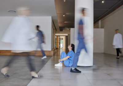 A worried nurse sits on the floor of a hospital