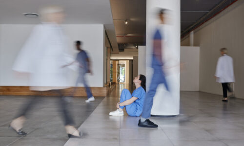 A worried nurse sits on the floor of a hospital