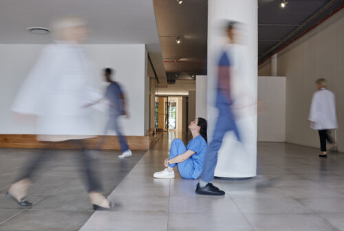 A worried nurse sits on the floor of a hospital
