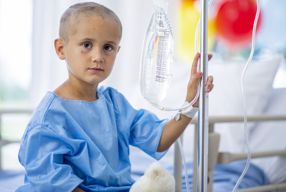 A young boy with cancer is indoors in a hospital.