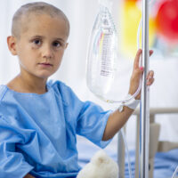 A young boy with cancer is indoors in a hospital.
