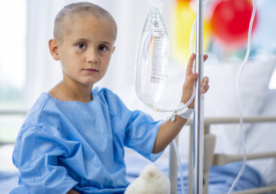 A young boy with cancer is indoors in a hospital.