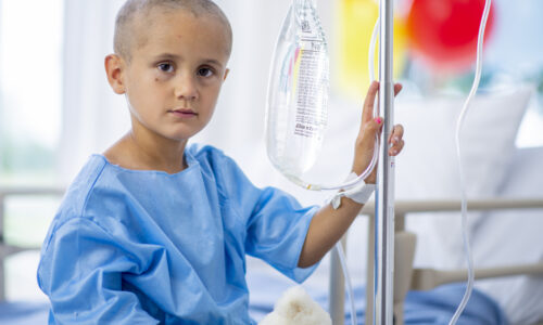 A young boy with cancer is indoors in a hospital.