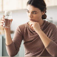 A woman holding and examining a glass of water