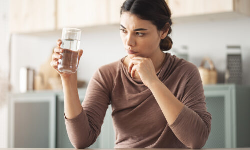 A woman holding and examining a glass of water