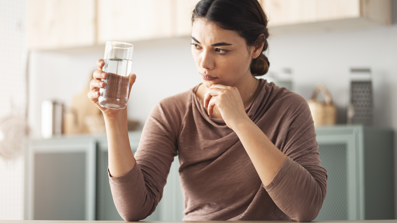 A woman holding and examining a glass of water